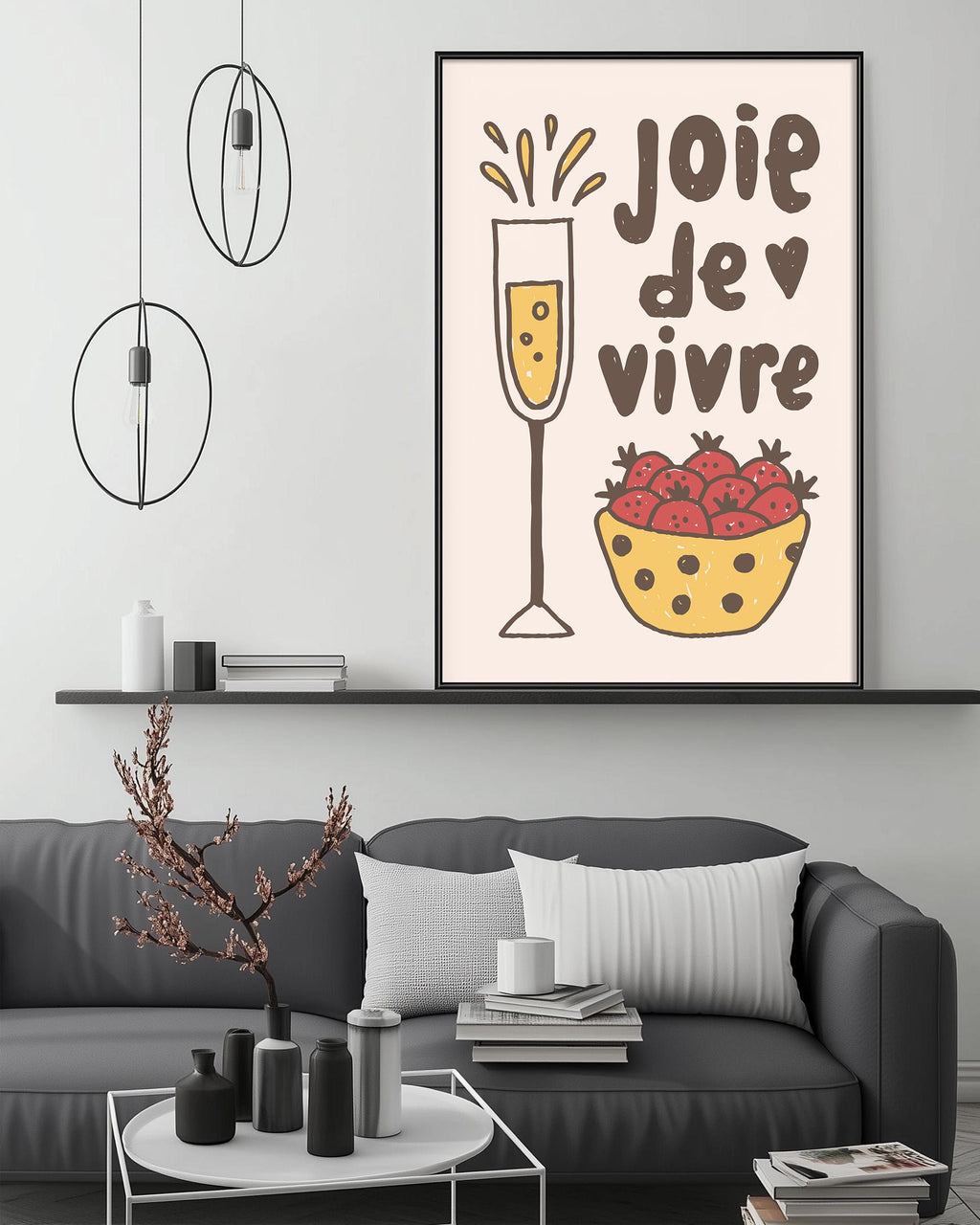 a living room with a gray couch, a coffee table, and a framed poster on the wall. The poster has a whimsical illustration of a glass of champagne and a bowl of strawberries, accompanied by the text "JOIE DE VIVRE" which translates to "Happy Vivid".