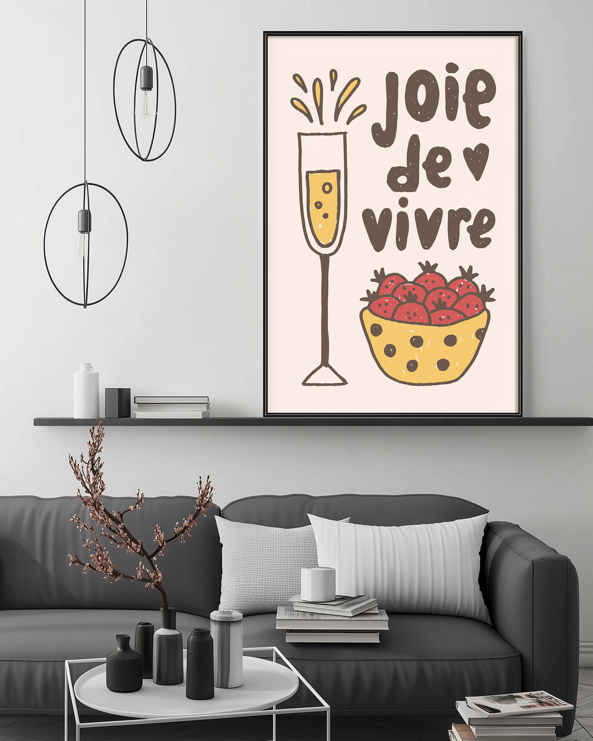 a living room with a gray couch, a coffee table, and a framed poster on the wall. The poster has a whimsical illustration of a glass of champagne and a bowl of strawberries, accompanied by the text "JOIE DE VIVRE" which translates to "Happy Vivid".