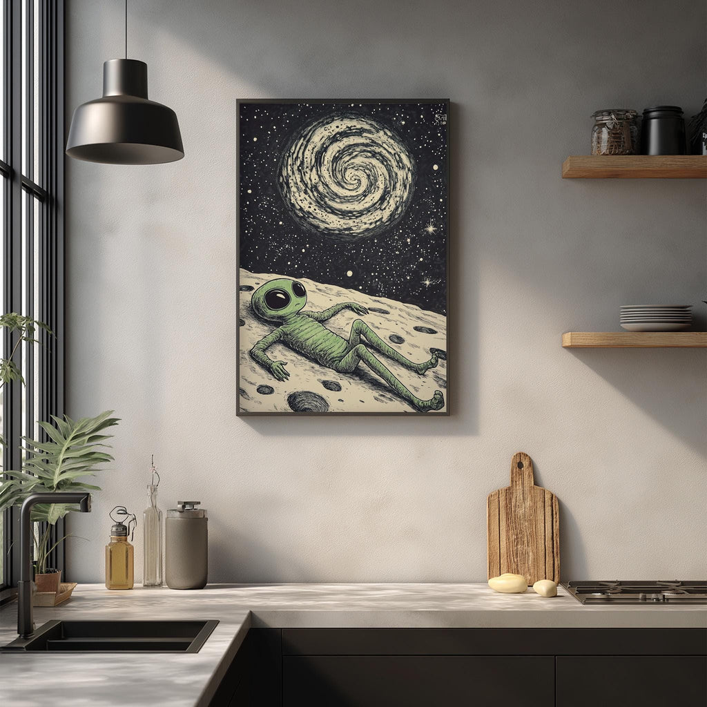 a framed artwork depicting an alien lying on a surface, with a spiral galaxy in the background. The artwork is hanging on a wall above a kitchen counter with various kitchen items, such as a cutting board, a bottle, and a bowl.
