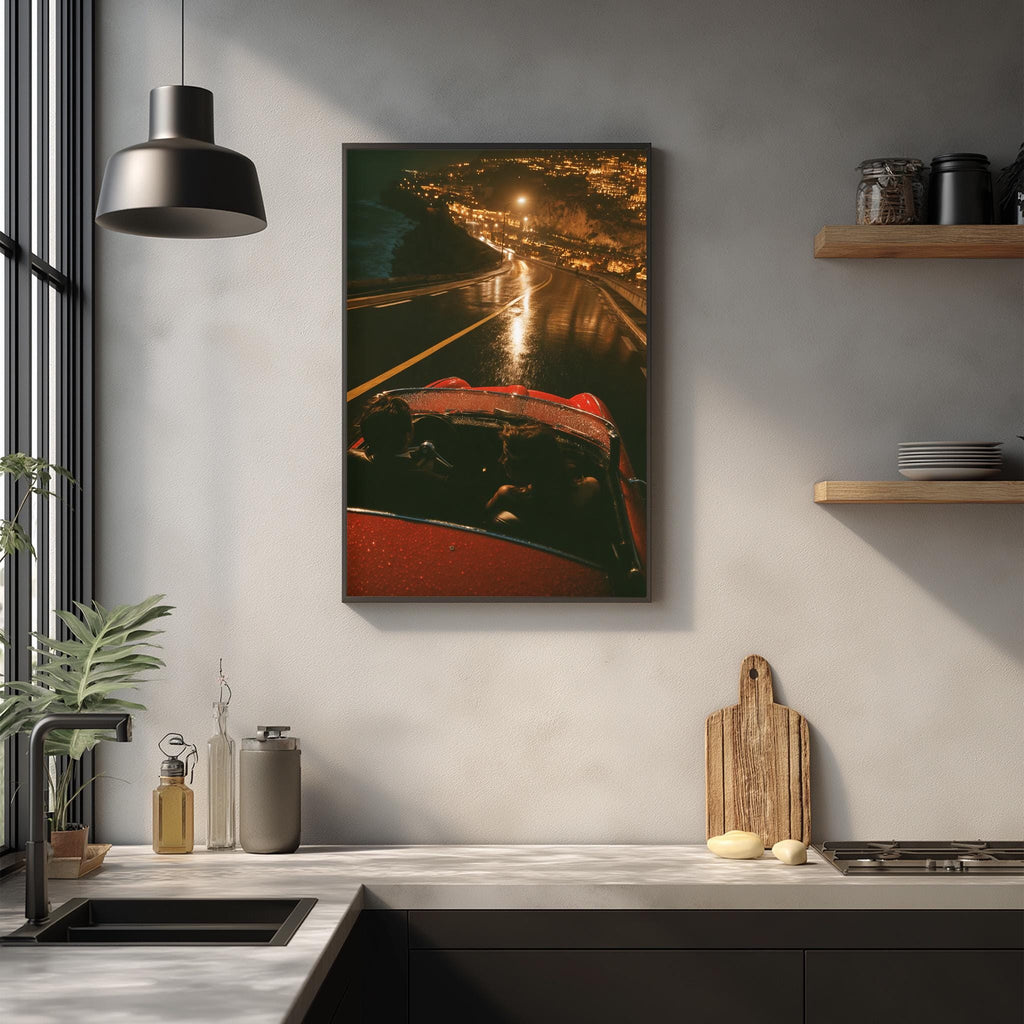 a kitchen counter with various items on it, including a red car, a cutting board, and some bottles. Above the counter, there is a framed picture hanging on the wall, depicting a nighttime cityscape with a car driving down a road.