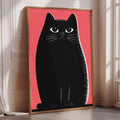 A large framed poster of a black cat with a pink background, sitting on a wooden floor.