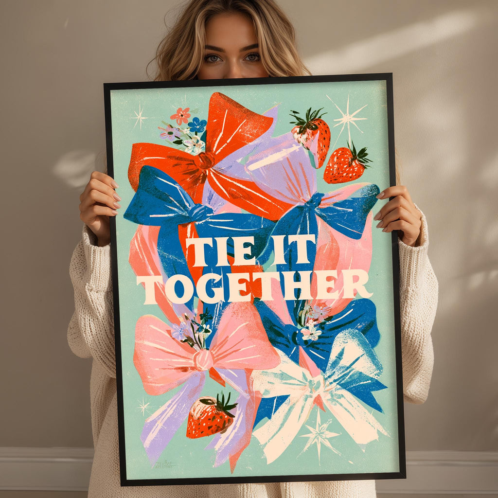 A woman holding a framed poster with a colorful design featuring bows, flowers, and strawberries.