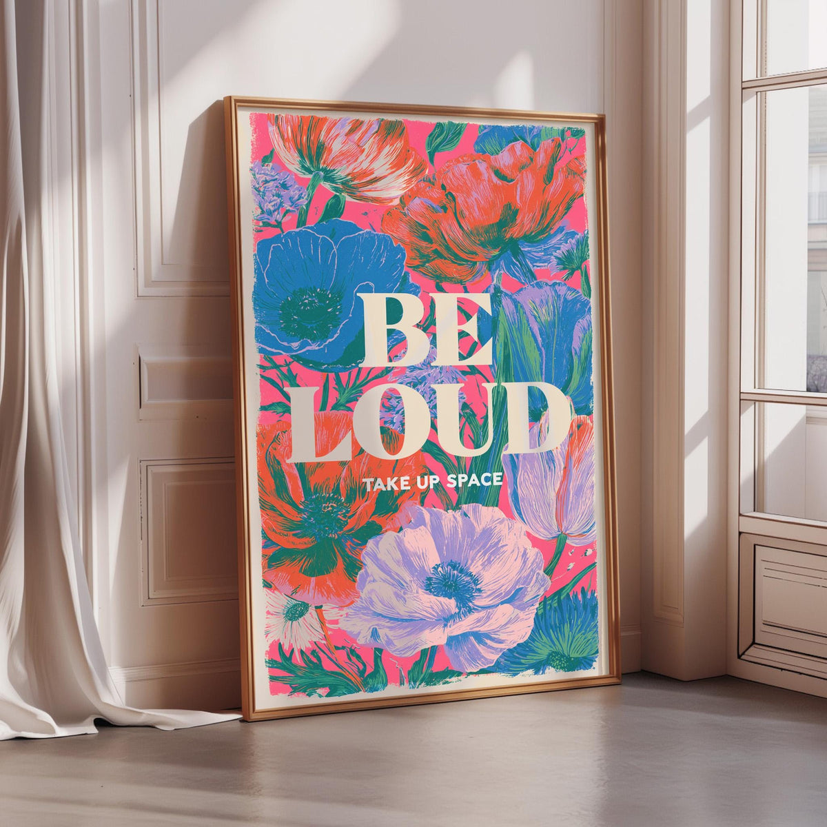 A framed poster with a vibrant floral design and the text "BE LOUD TAKE UP SPACE" is displayed on a wall.