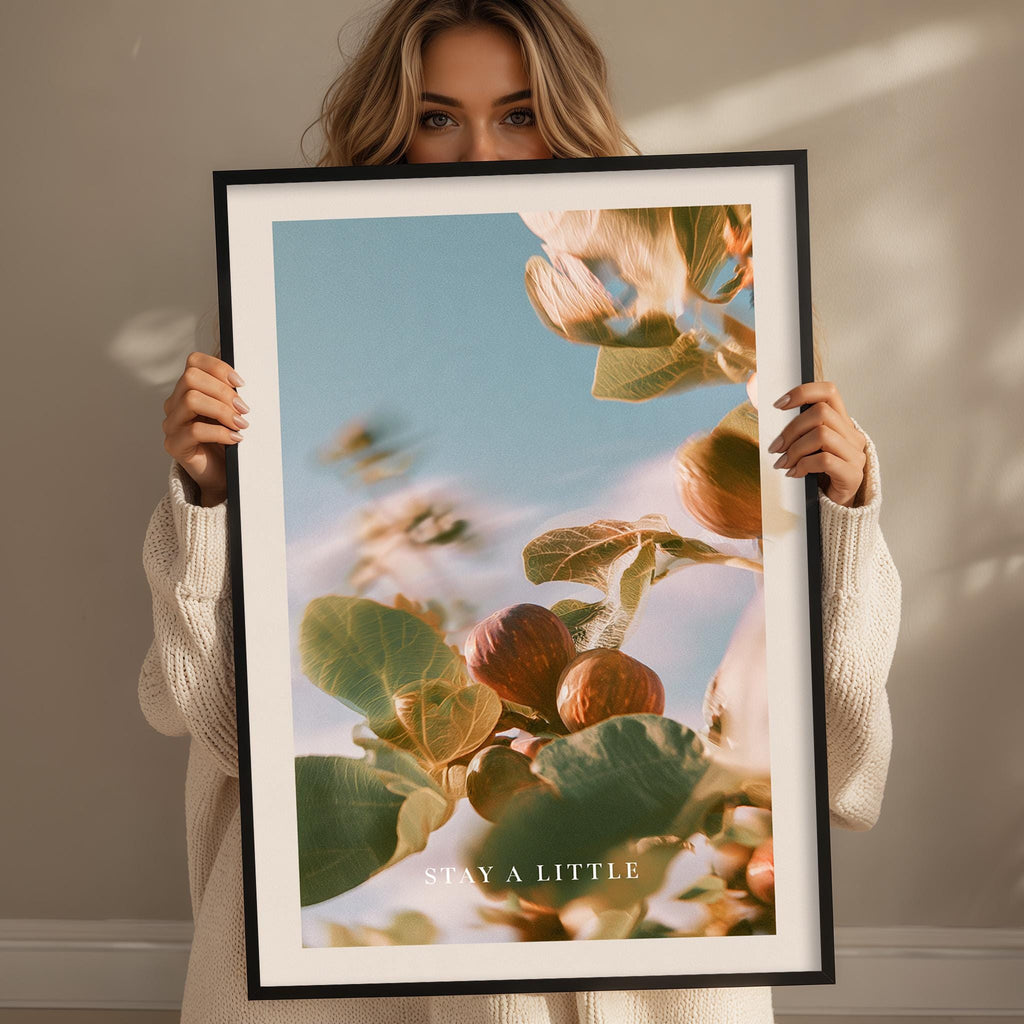 A woman holding a framed print with a close-up of a plant with leaves and fruits.
