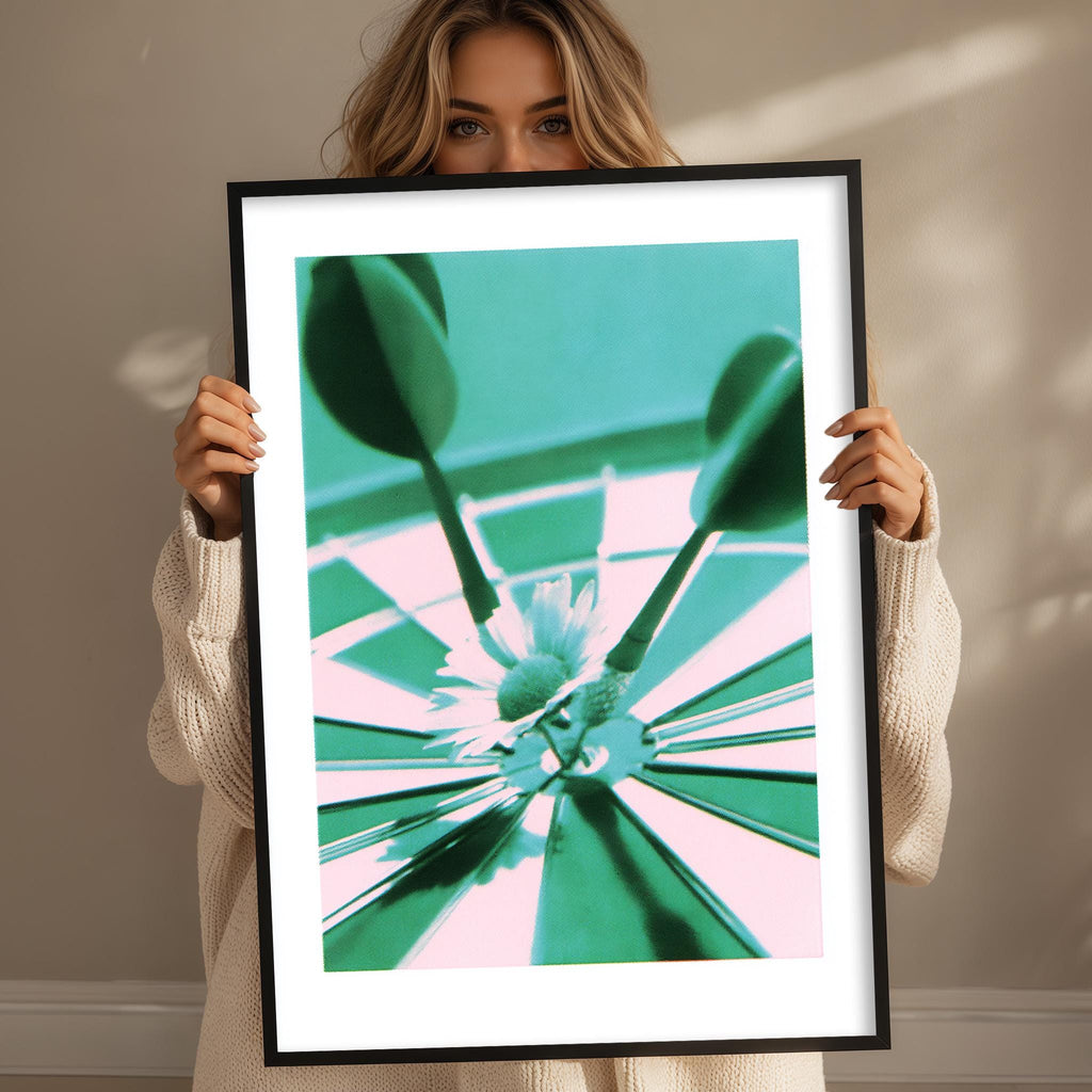 A woman holds a framed photograph of a green and pink target with a white flower in the center.