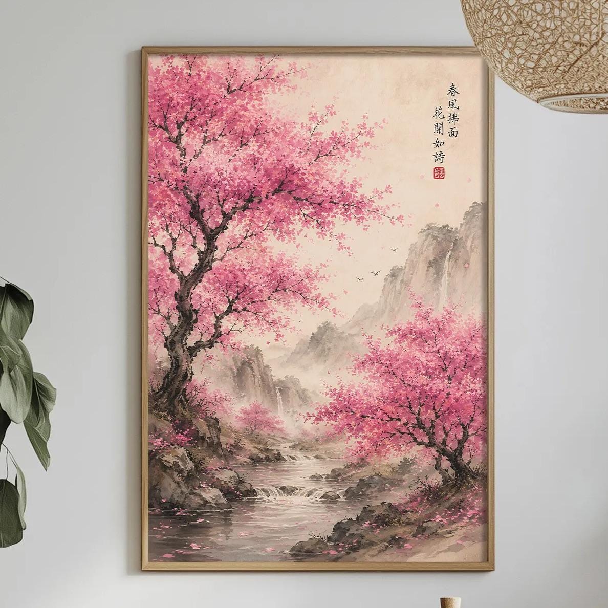 a serene indoor setting with a framed painting of a pink flowering tree on the wall, a dining table with a bottle, a bowl, and a vase of flowers, and potted plants in the background.