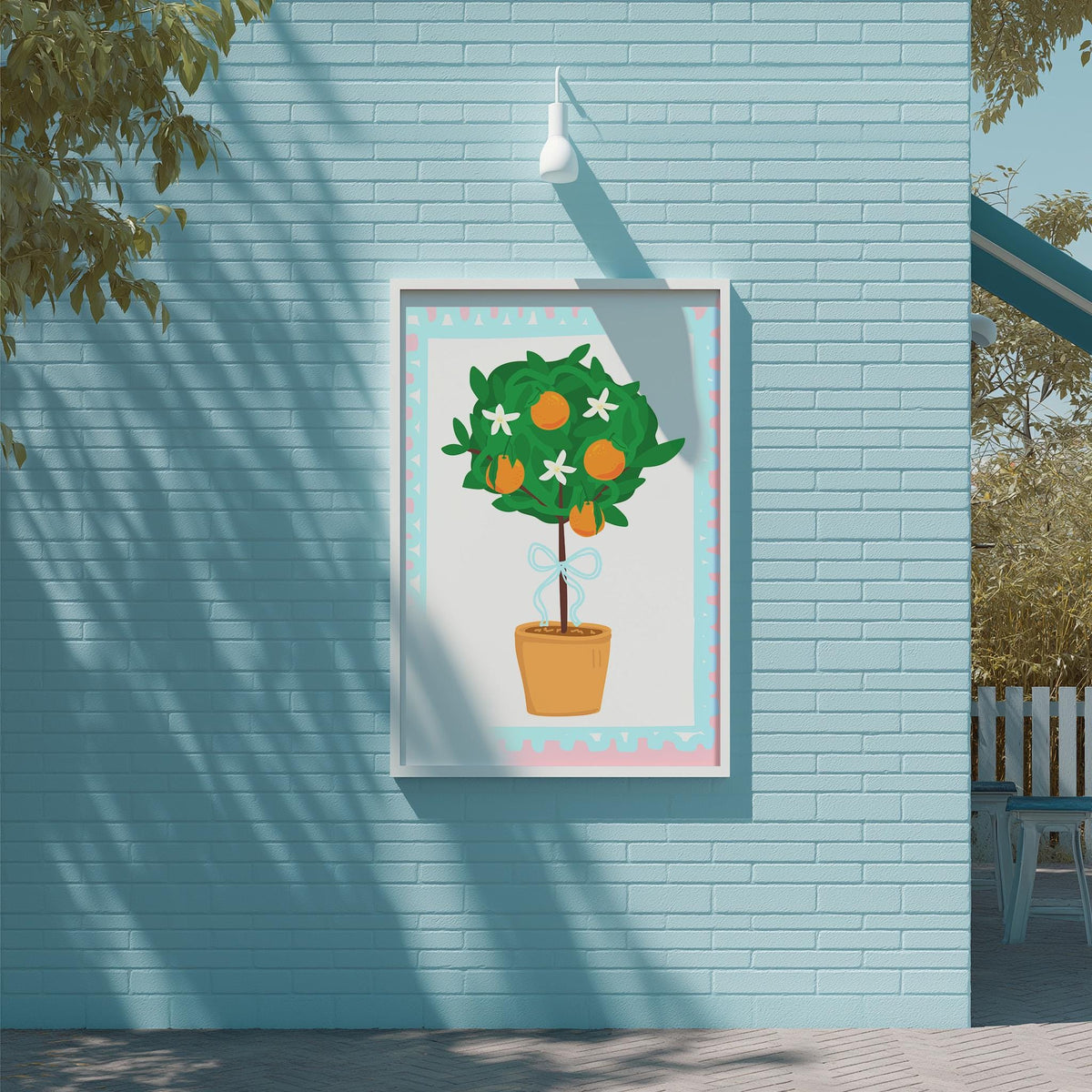 A framed illustration of a potted tree with orange flowers is displayed on a blue brick wall.