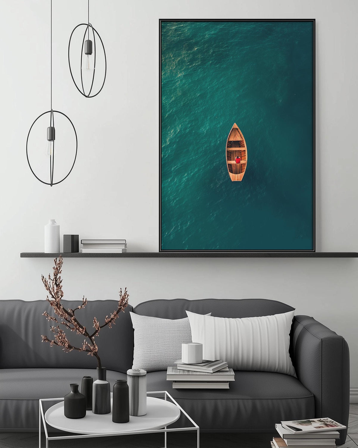 a large black and white photograph of a boat floating on a turquoise ocean, hanging on a wall above a gray couch with white pillows.