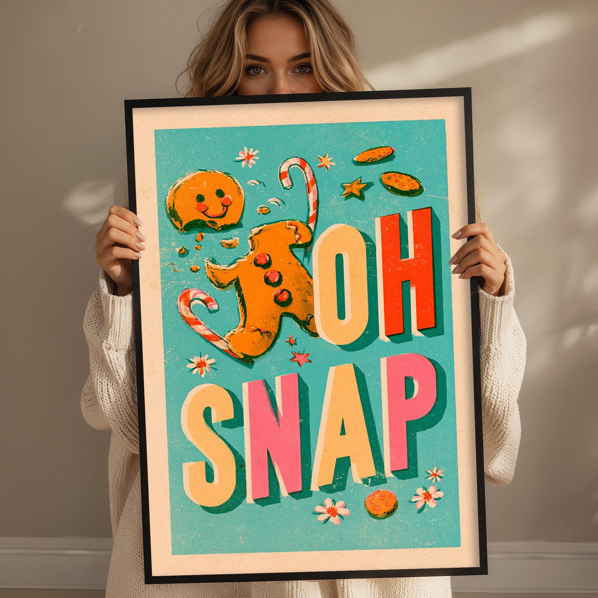 A woman is holding up a framed poster with a colorful design featuring a gingerbread man and the text "OH SNAP" in large letters.