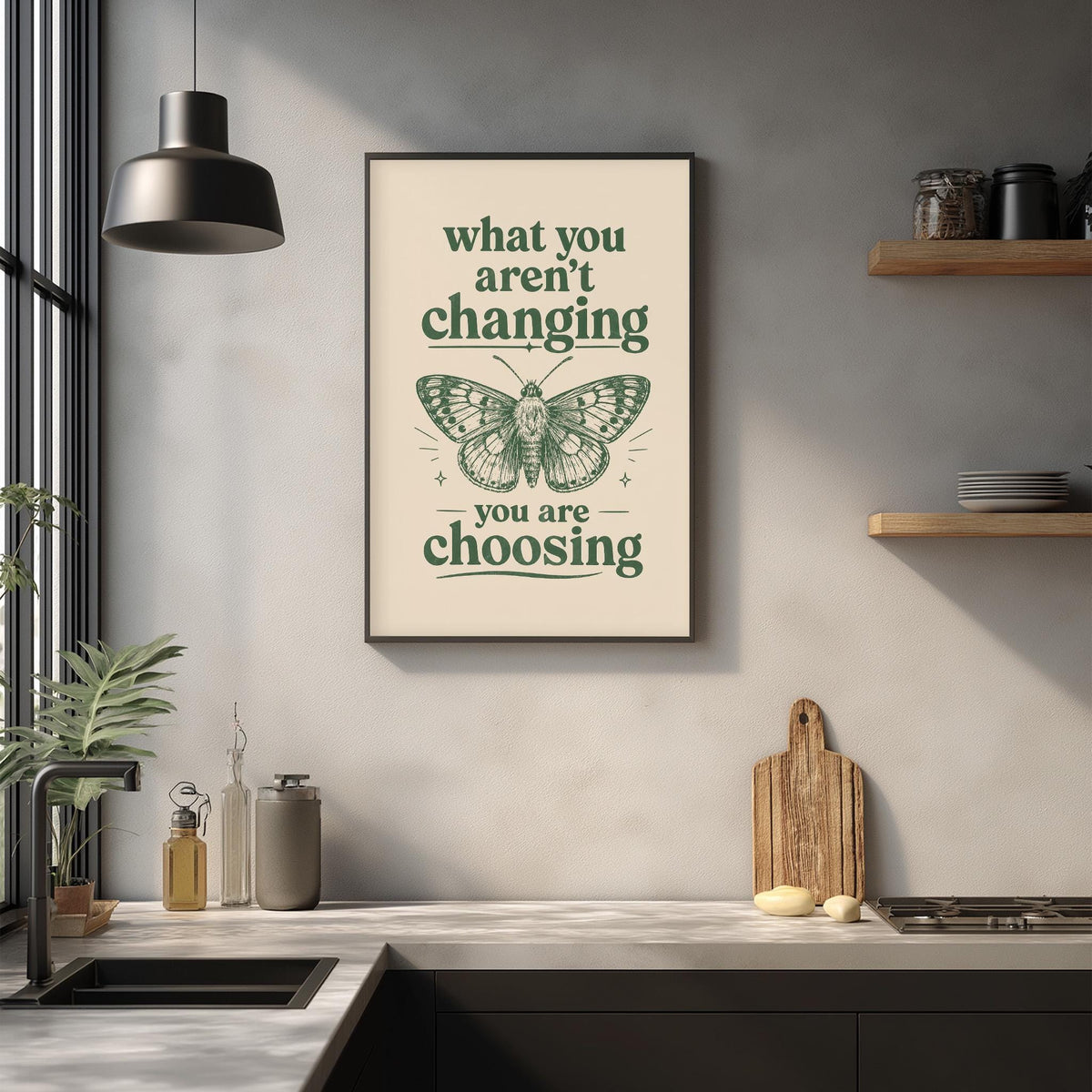 a framed poster with the text "What you aren't changing, you are choosing" and an illustration of a butterfly. The poster is displayed on a wall above a kitchen counter with various kitchen items such as a cutting board, a knife, and a bottle.