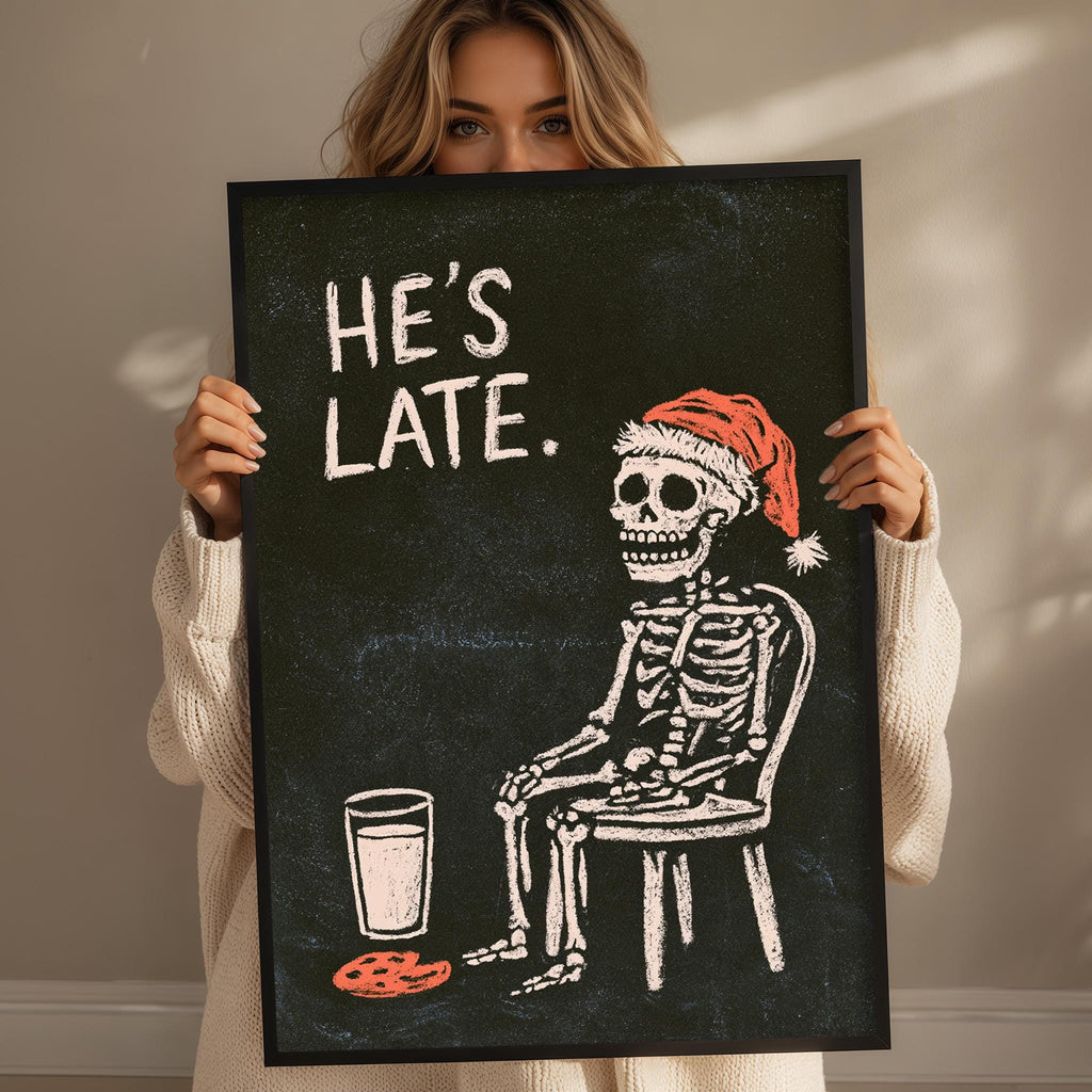 A woman is holding up a framed image that depicts a skeleton wearing a Santa hat and sitting in a chair, with a glass of milk next to it.