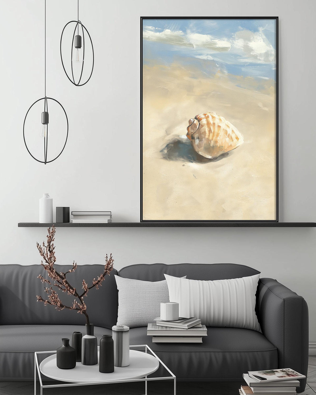 a large framed painting of a shell resting on a sandy beach, hanging on a wall above a gray couch with white pillows.