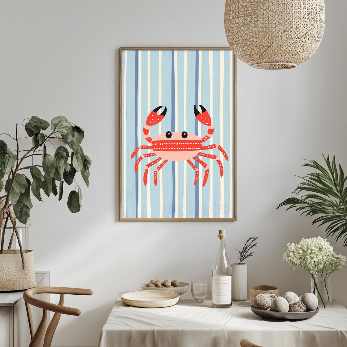 a dining table with a white tablecloth, a bowl of fruit, a bottle, and a vase with flowers. Above the table, there is a framed picture of a red crab with a blue and white striped background.