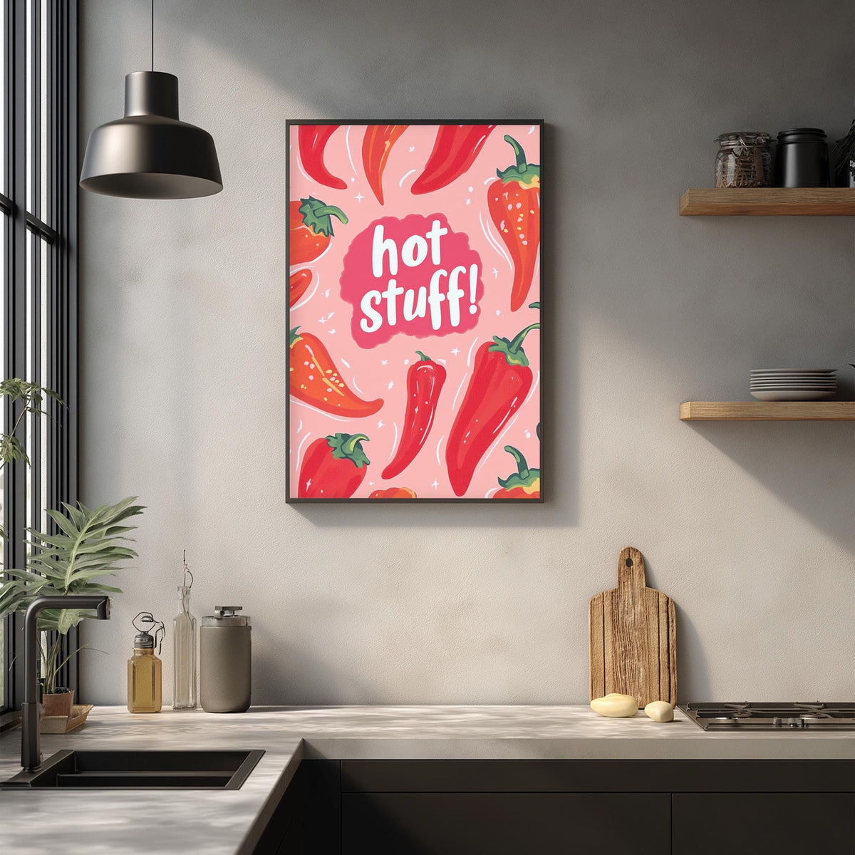 a kitchen counter with various kitchen items, including a cutting board, a bottle, and a jar. Above the counter, there is a framed poster with a pink background and red peppers, along with the text "hot stuff!"