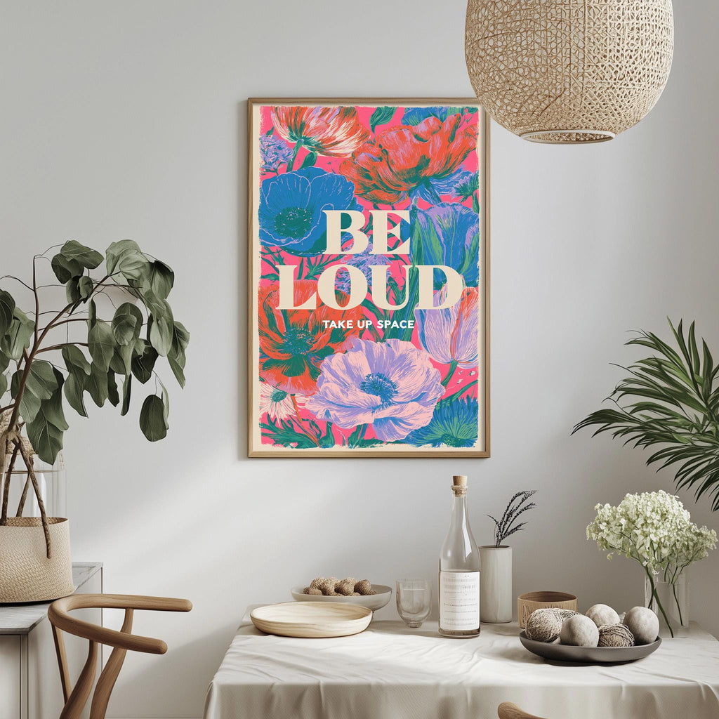 a framed poster with a vibrant floral design hanging on a wall above a dining table with various decorative items and plants.
