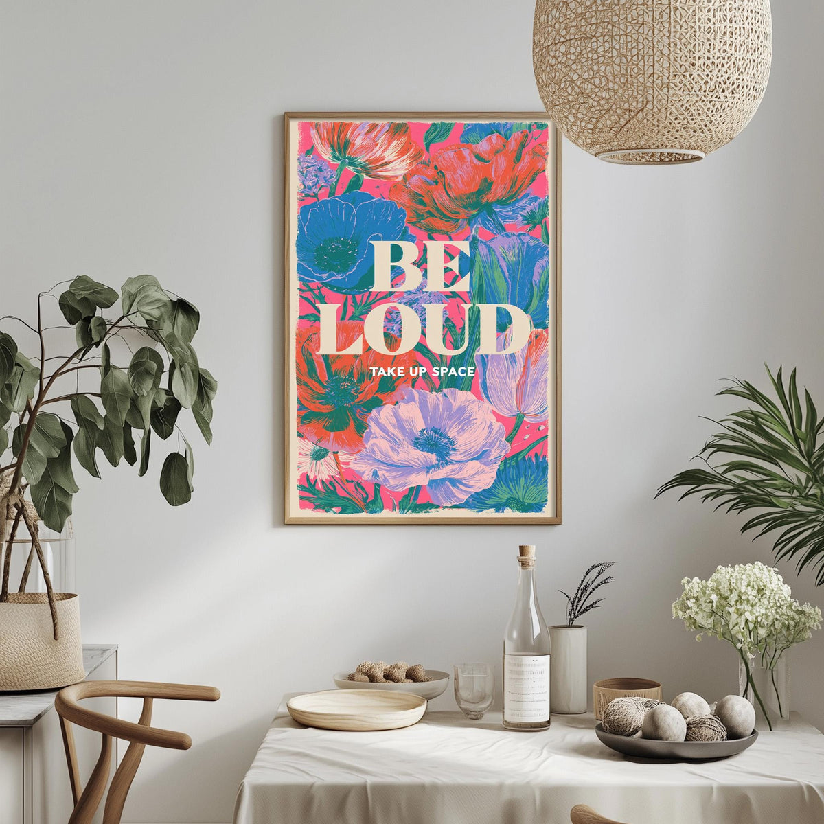 a framed poster with a vibrant floral design hanging on a wall above a dining table with various decorative items and plants.