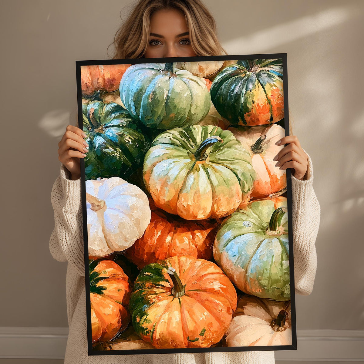 A woman holds up a framed print of a vibrant collection of pumpkins, showcasing a variety of colors and sizes.