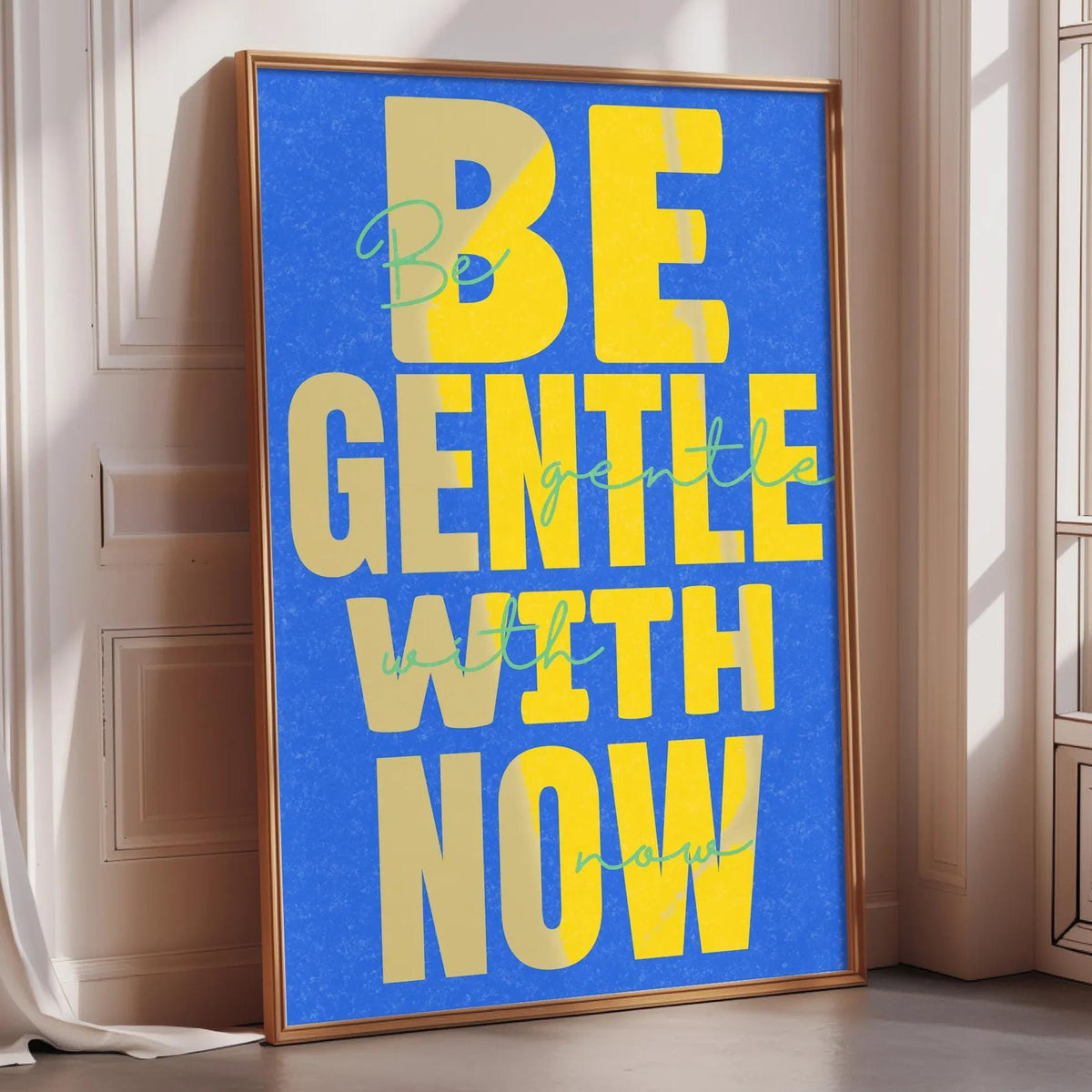 A framed poster with the text "BE GENTLE WITH NOW" displayed prominently on it.