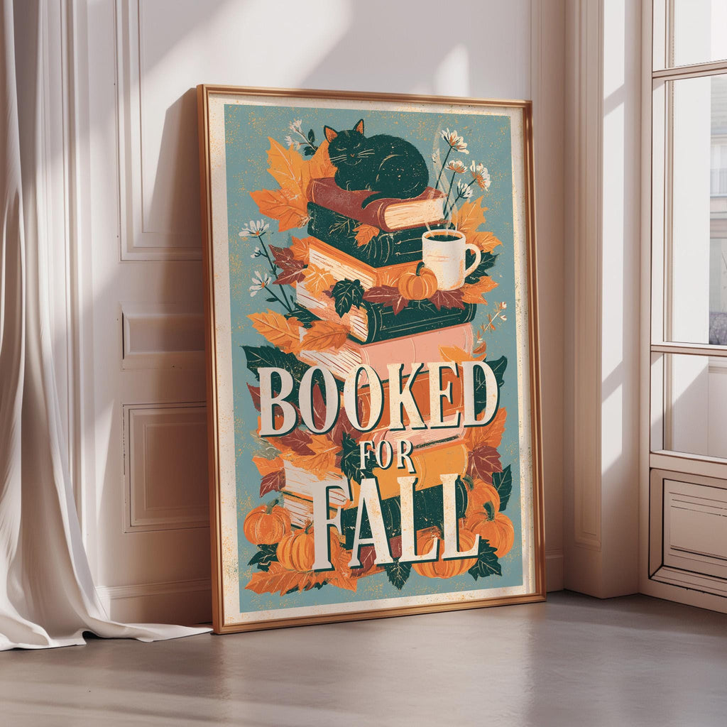 A framed poster with a cat sitting on top of a stack of books, surrounded by autumn leaves, flowers, and a cup of coffee. The text on the poster reads "BOOKED FOR FALL".