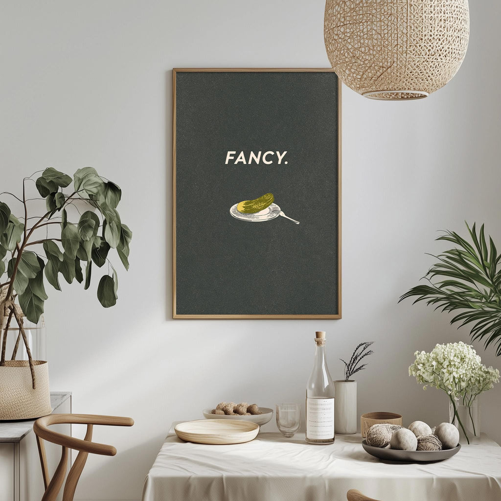 a dining table with a white tablecloth, a bowl of fruit, a bottle, and a vase with flowers. Above the table, there is a framed poster with the word "FANCY" written on it.