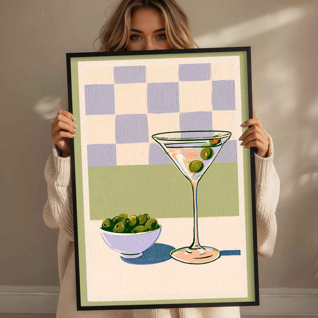 A woman holding a framed picture of a martini glass with olives and a bowl of olives.