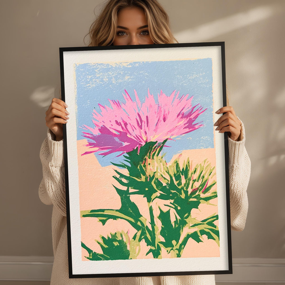 A woman is holding up a framed print of a colorful painting depicting a vibrant pink flower with green leaves.