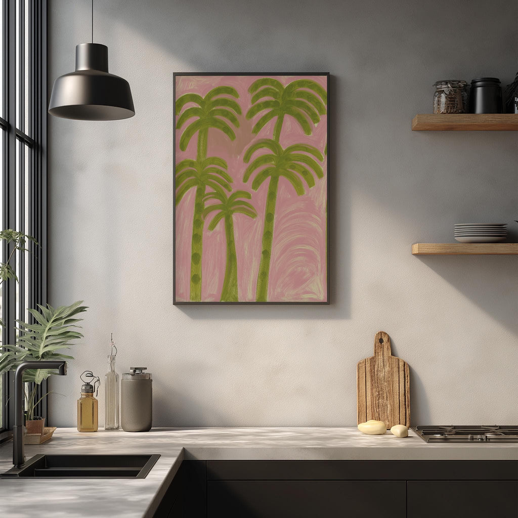 a kitchen counter with a framed painting of palm trees hanging above it. The painting has a pink background and green palm trees. On the counter, there are various kitchen items such as a cutting board, a knife, and a bottle. The kitchen also has a window and a shelf with dishes on it.