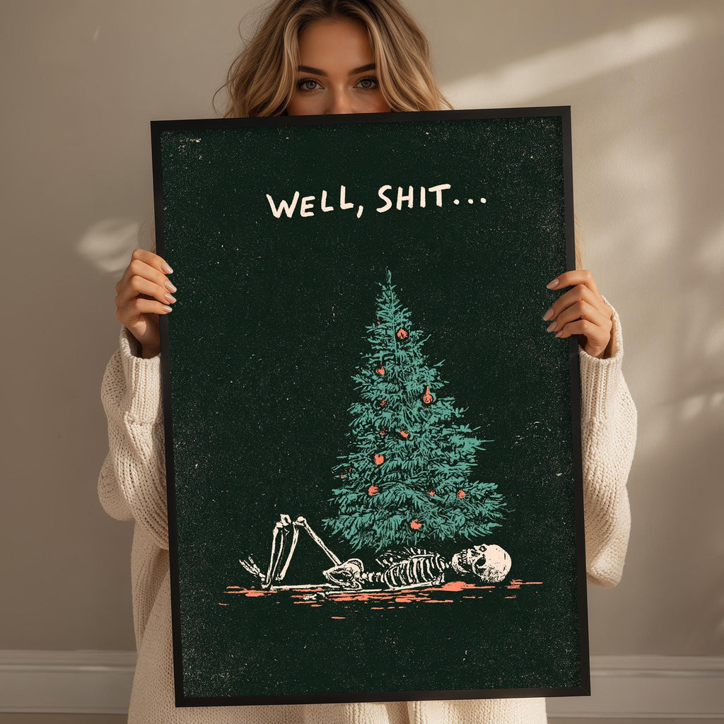 A woman holding a framed poster with a graphic of a skeleton lying on the ground next to a Christmas tree.