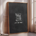 A large blackboard with a stack of books on it, and the text "JUST ONE MORE" written on it.