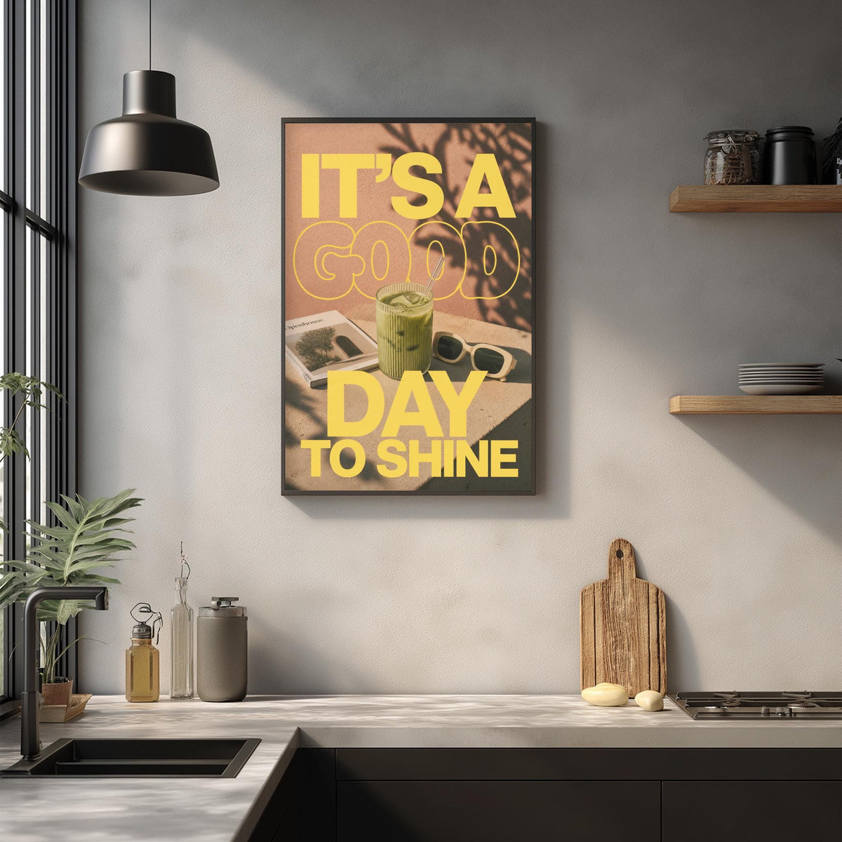 a kitchen counter with various items such as a cutting board, a blender, and a plant. Above the counter, there is a framed poster with the text "IT'S A GOOD DAY TO SHINE" displayed prominently.