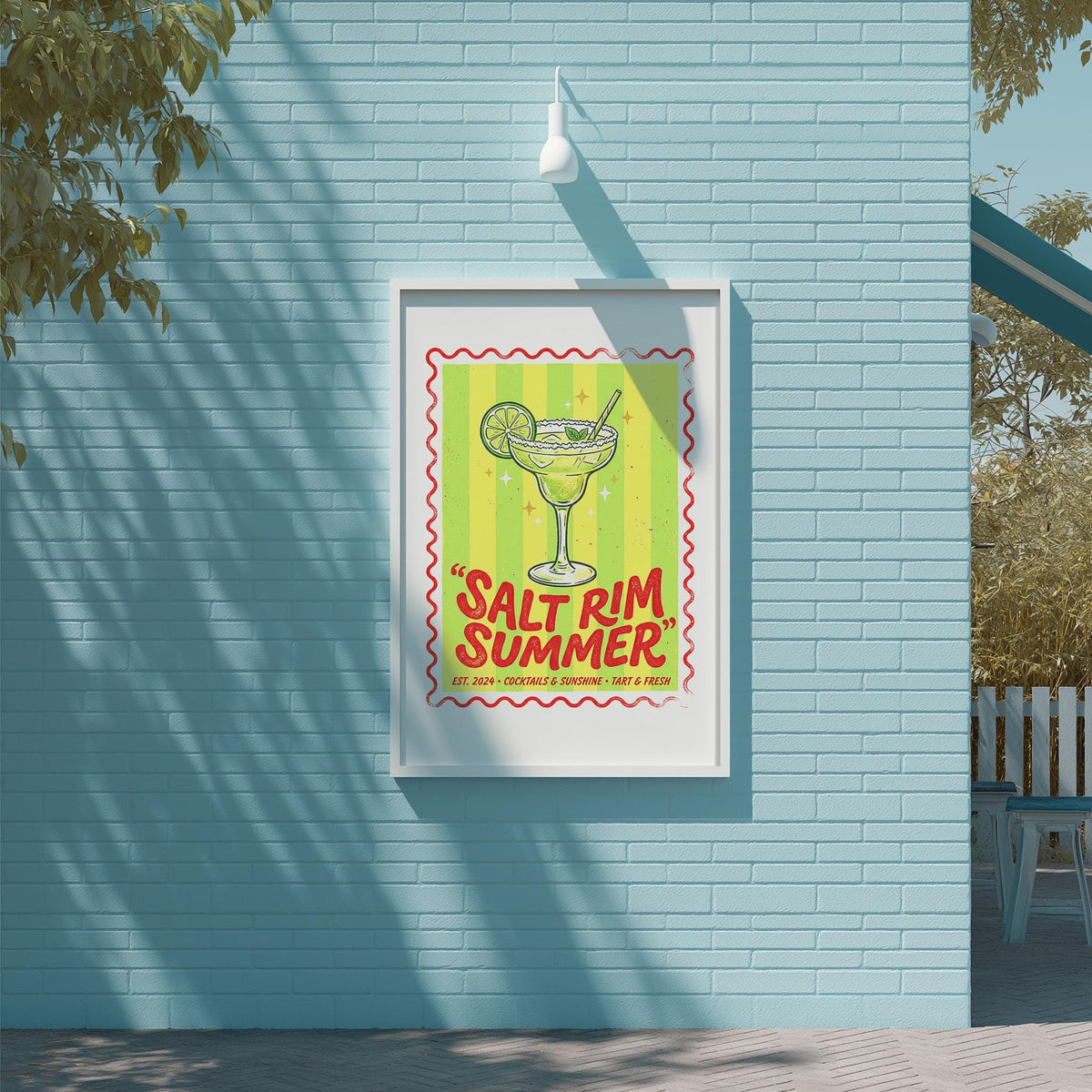 A framed poster with a vibrant illustration of a margarita glass and the text "Salt rim summer" is displayed on a blue brick wall.