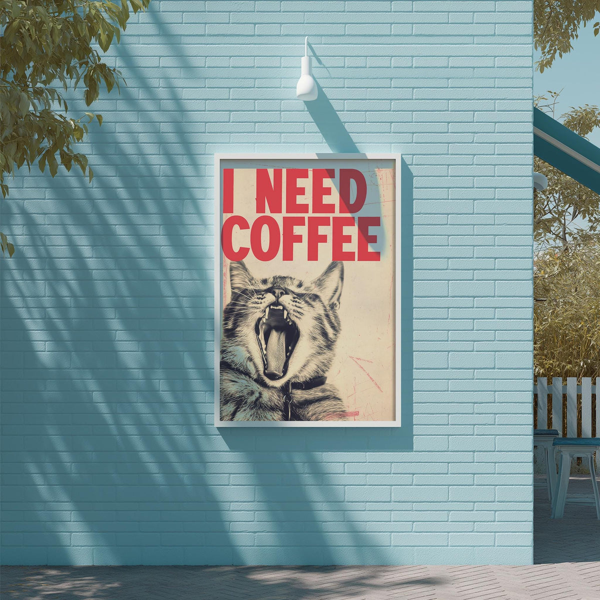 A framed poster with a cat's face and the text "I NEED COFFEE" is displayed on a blue brick wall.