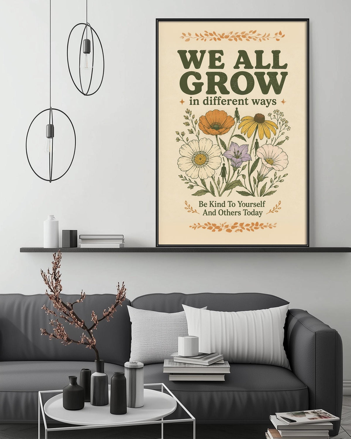a poster with the text "WE ALL GROW in different ways" and an illustration of flowers, hanging on a wall above a gray couch with a coffee table in front of it.