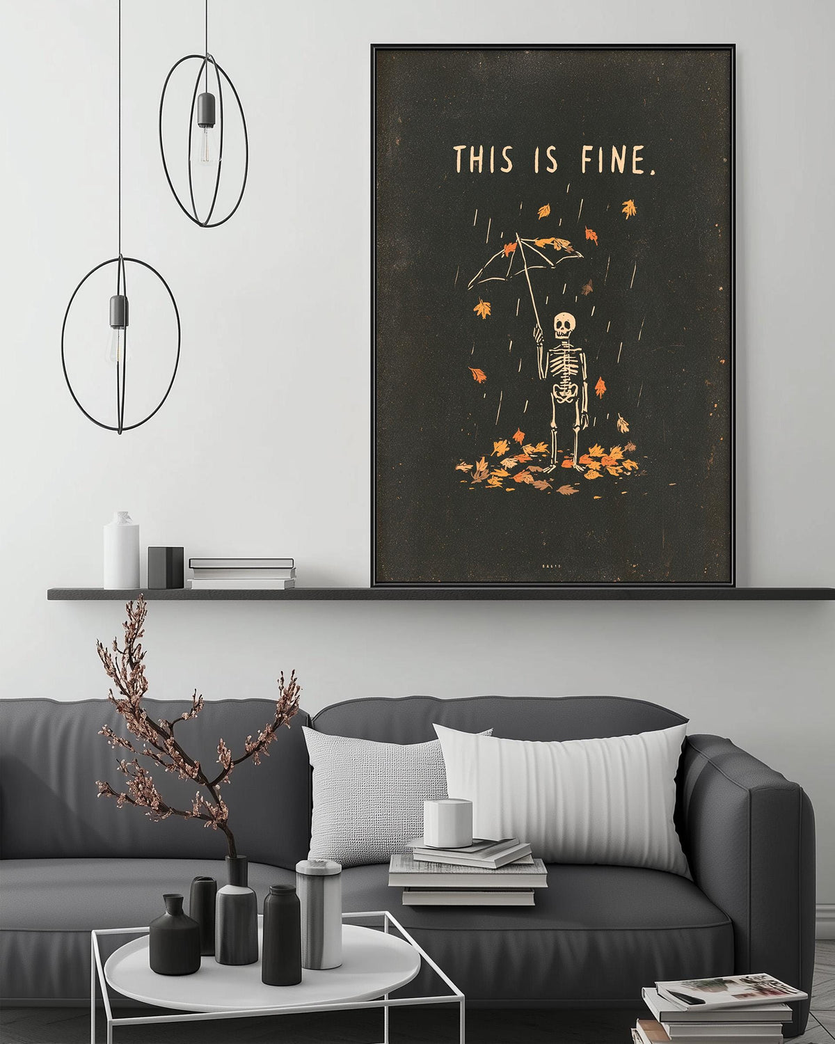a living room with a gray sofa, a coffee table, and a large framed poster on the wall. The poster depicts a skeleton holding an umbrella and surrounded by falling leaves, with the text "THIS IS FINE."