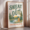 a framed poster with a scenic landscape and the text "SWEAT IT OUT" prominently displayed.