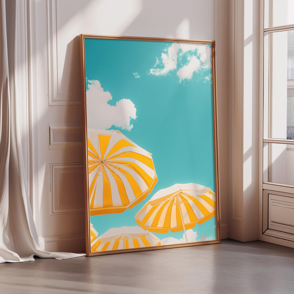 A framed poster of a bright blue sky with fluffy white clouds and three yellow and white striped umbrellas in the foreground.