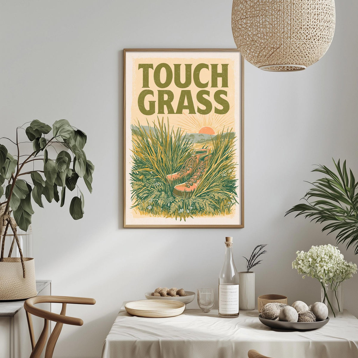 a framed poster of a grassy field with a sun and a pair of shoes, hanging on a wall above a dining table with various items on it.