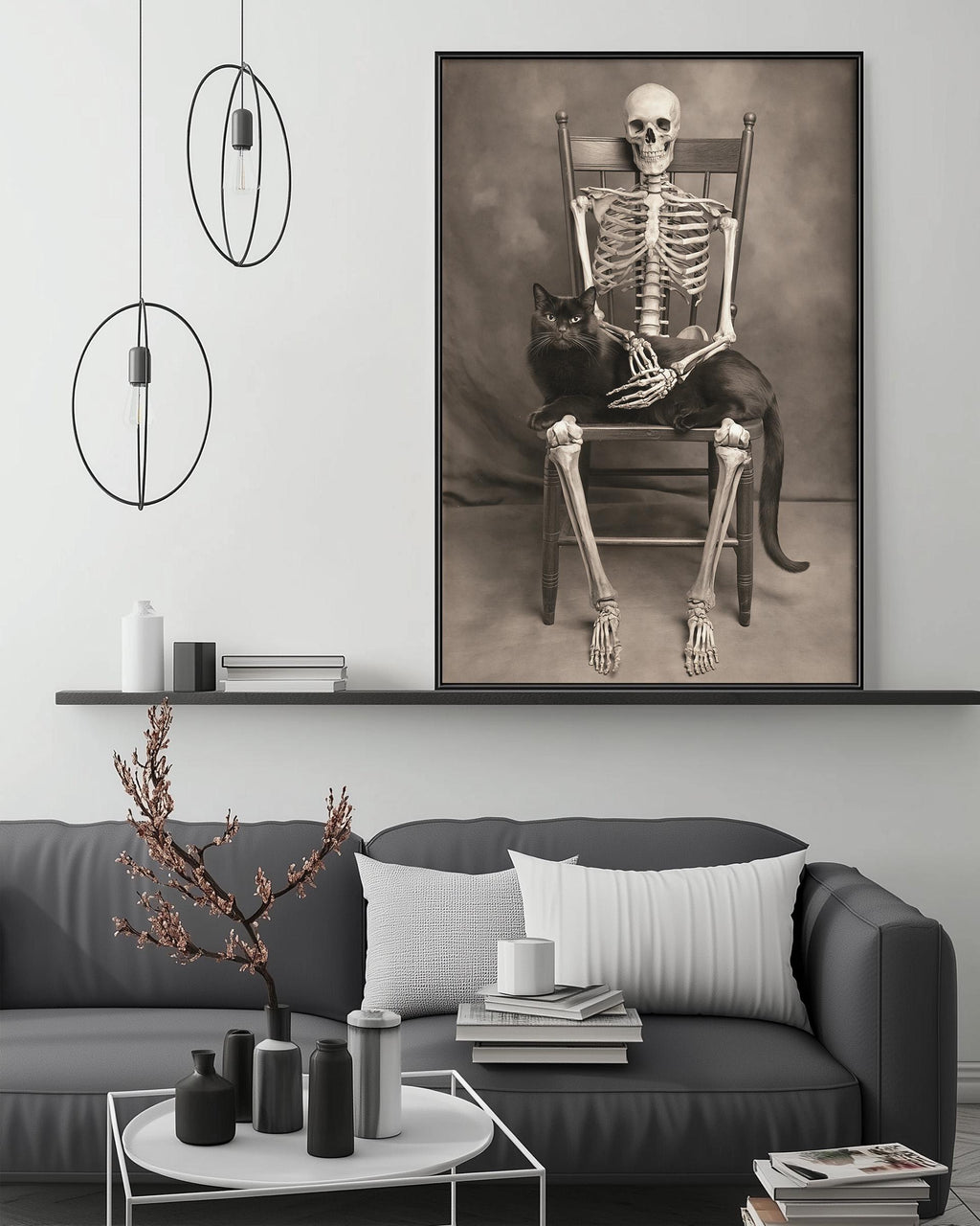 a black and white photograph of a skeleton sitting in a chair, holding a cat in its lap. The photograph is displayed on a wall above a gray couch, which is decorated with various items such as a potted plant, vases, and books.