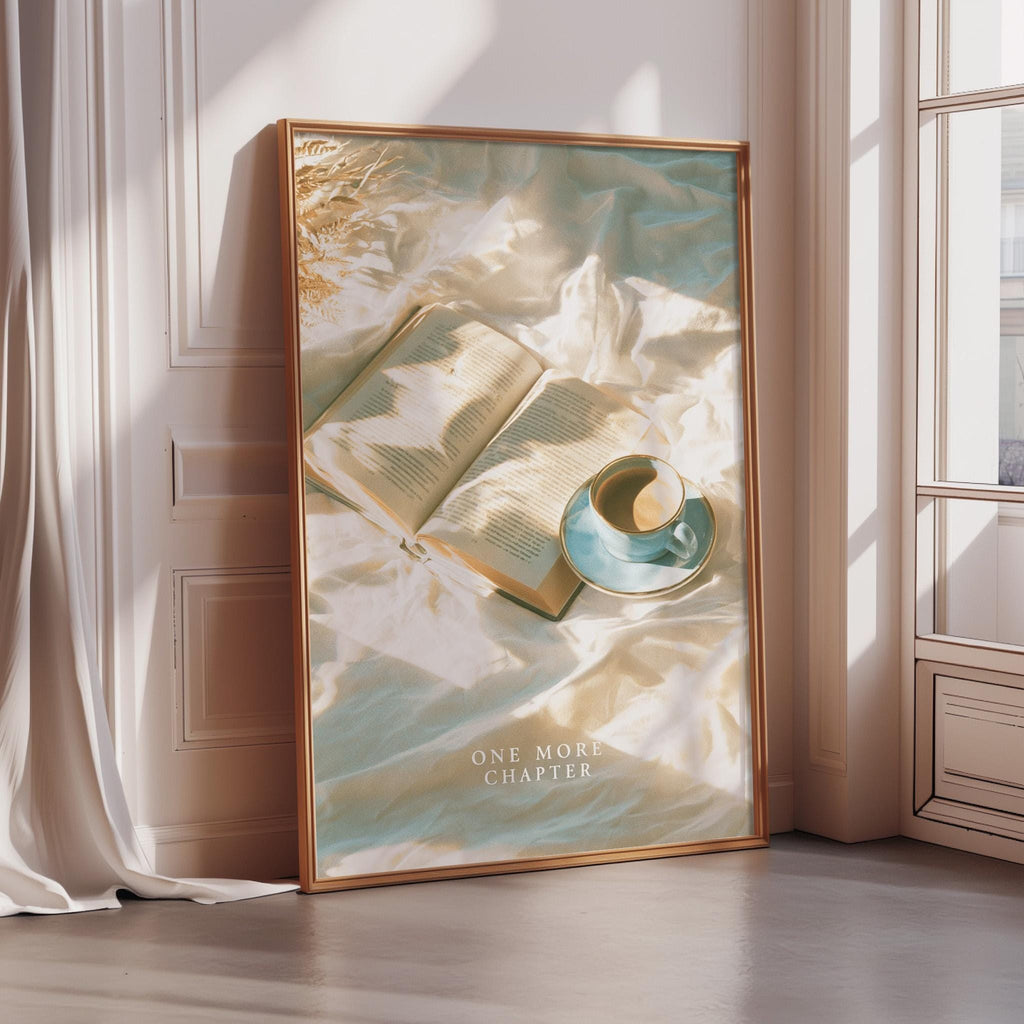 A framed poster with an open book and a cup of coffee on a bed, set against a white wall and a window.