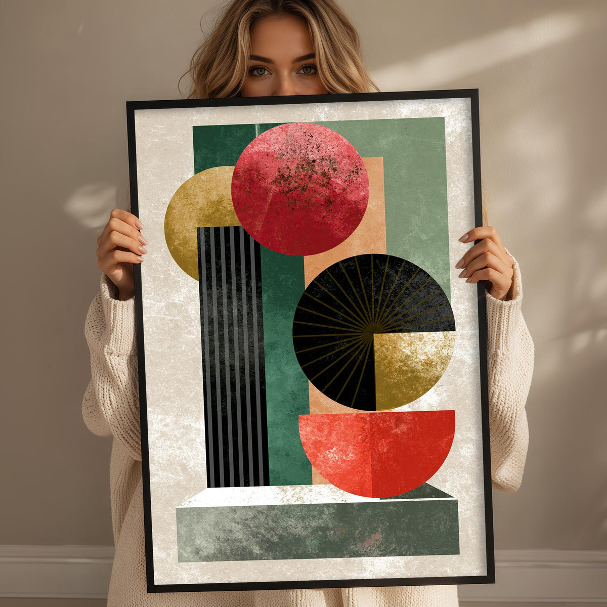 A woman is holding up a framed abstract art piece featuring geometric shapes in various colors, including red, green, and black.