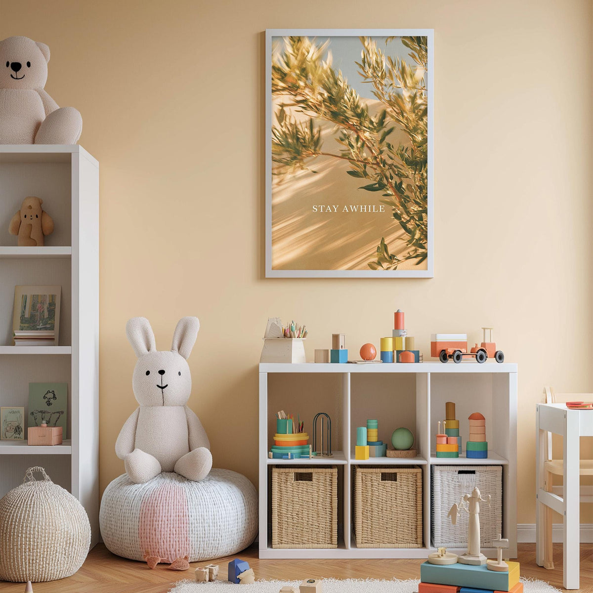 A cozy and colorful children's bedroom with a white bookshelf, a plush rabbit, and a toy train set. The walls are painted a light peach color, and a framed poster with the text "STAY AWHILE" is displayed above the bookshelf.