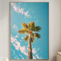 a large framed picture of a palm tree against a blue sky with clouds, hanging on a wall in a living room.
