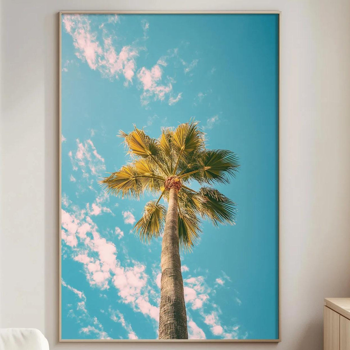 a large framed picture of a palm tree against a blue sky with clouds, hanging on a wall in a living room.