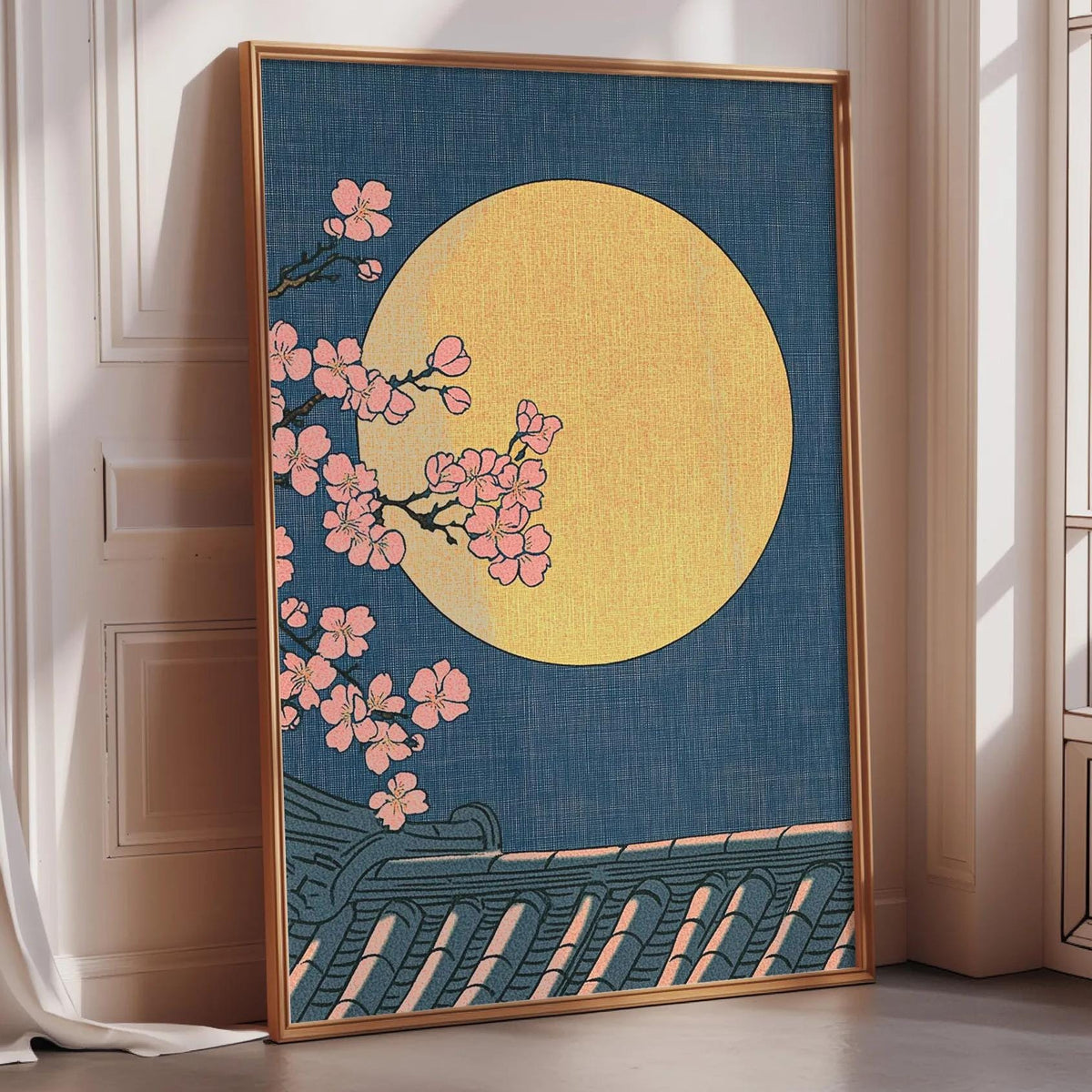 A framed artwork depicting a night scene with a large yellow moon and pink cherry blossoms against a dark blue background.