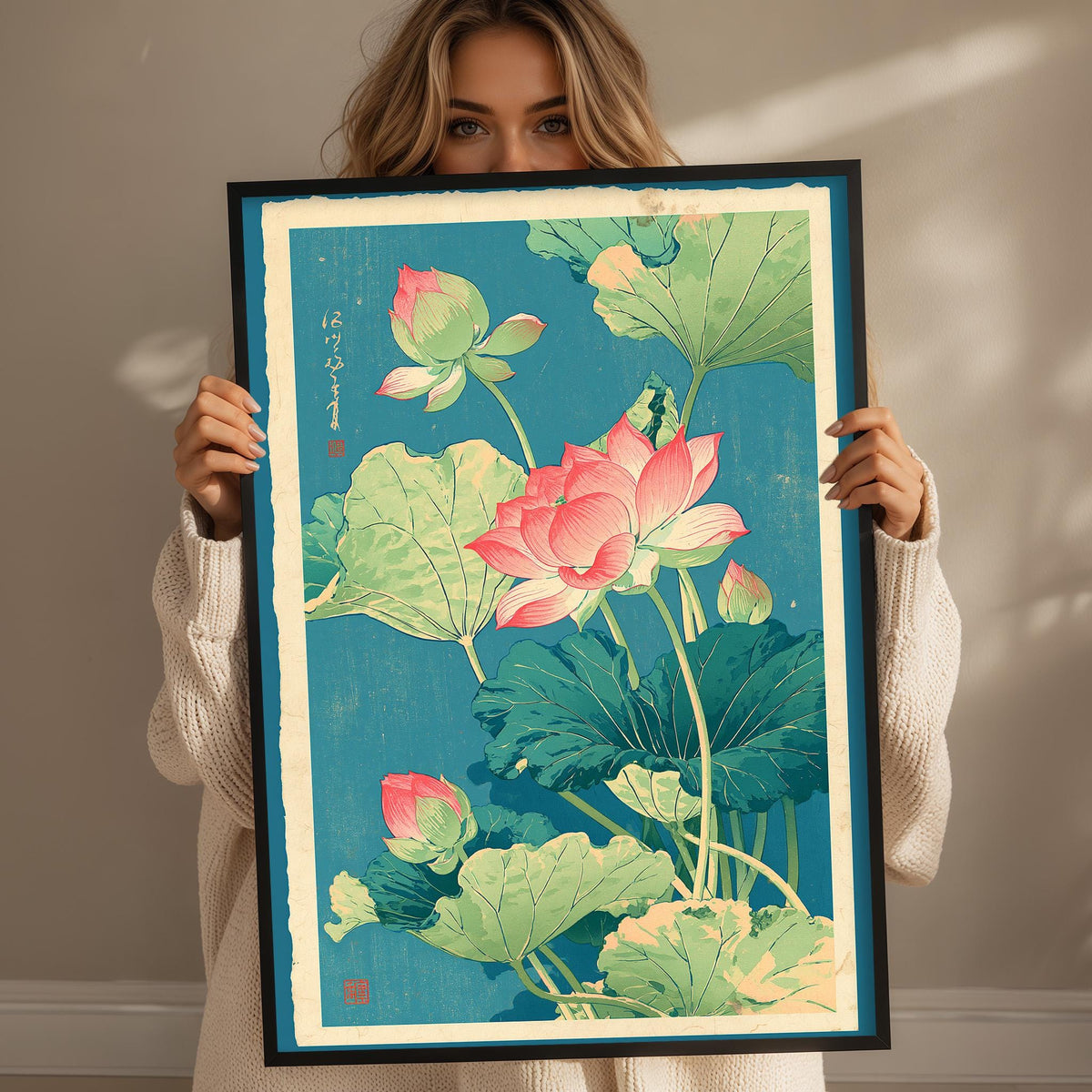 A woman is holding up a framed print of a vibrant illustration of lotus flowers in shades of pink, green, and blue.