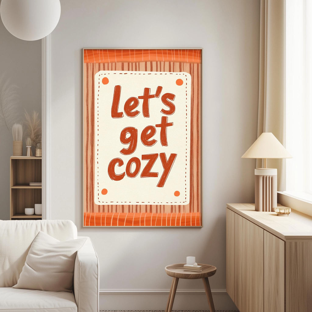 A cozy living room with a white sofa, a wooden side table, and a lamp. A framed poster with the text "Let's get cozy" is displayed on the wall.