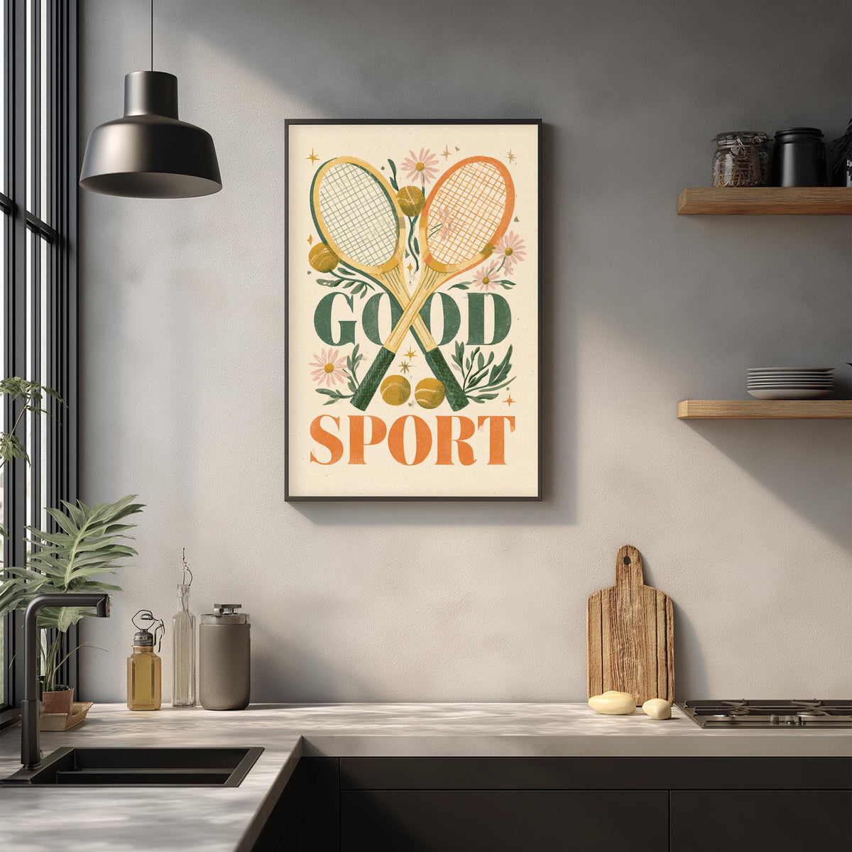 a framed poster with the text "GOOD SPORT" hanging on a wall above a kitchen counter with various kitchen items and a cutting board.