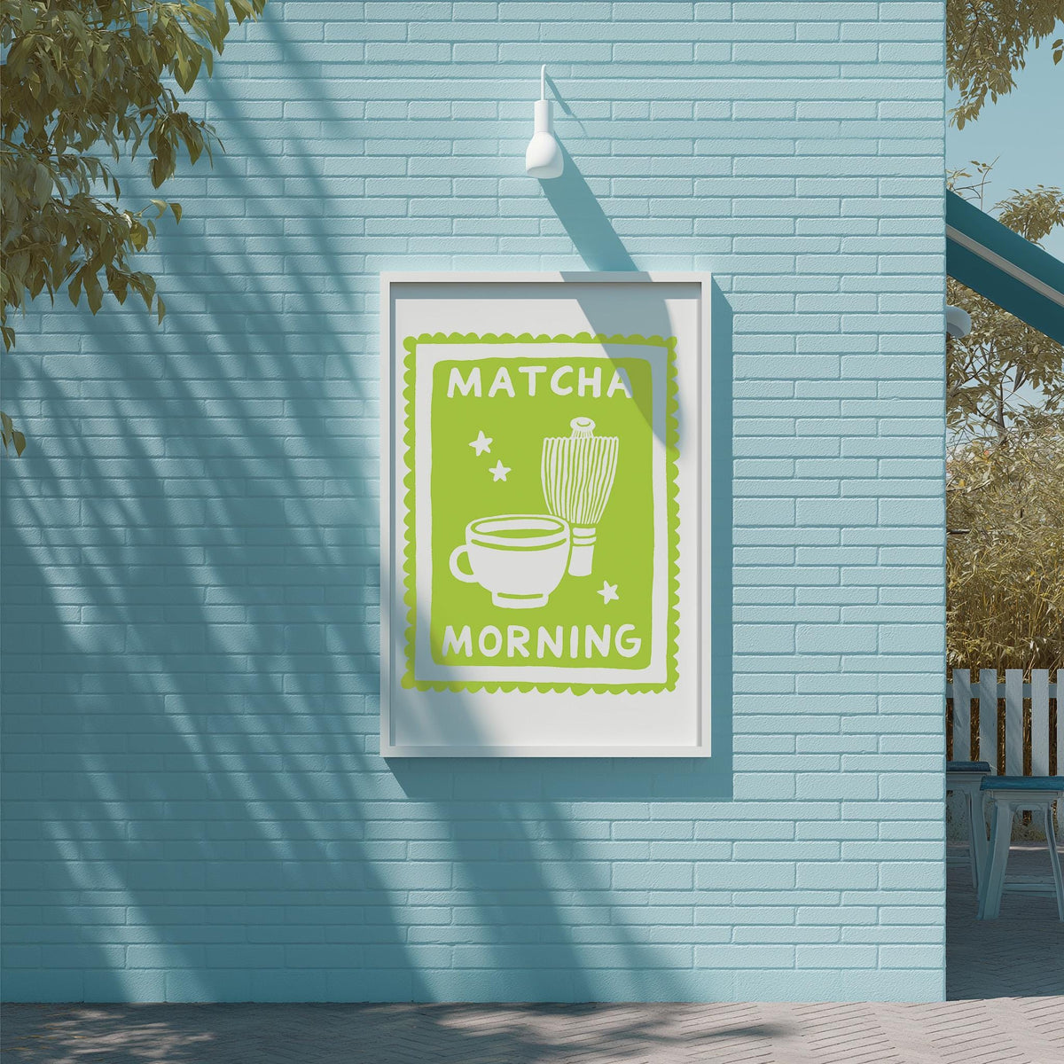 A framed poster with the text "MATCHA MORNING" and an illustration of a cup and a teapot, mounted on a blue brick wall.