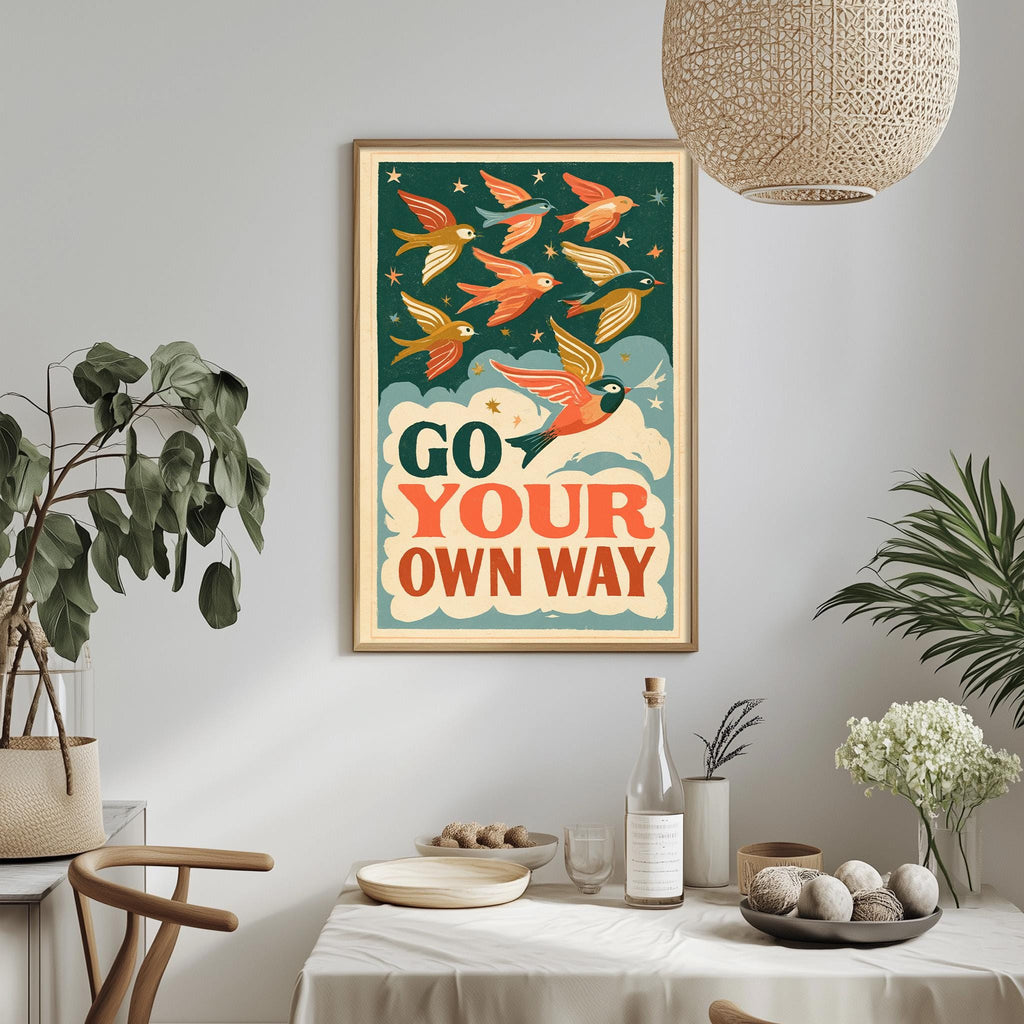 a framed poster with a bird illustration and the text "GO YOUR OWN WAY" hanging on a wall above a dining table with various items on it.