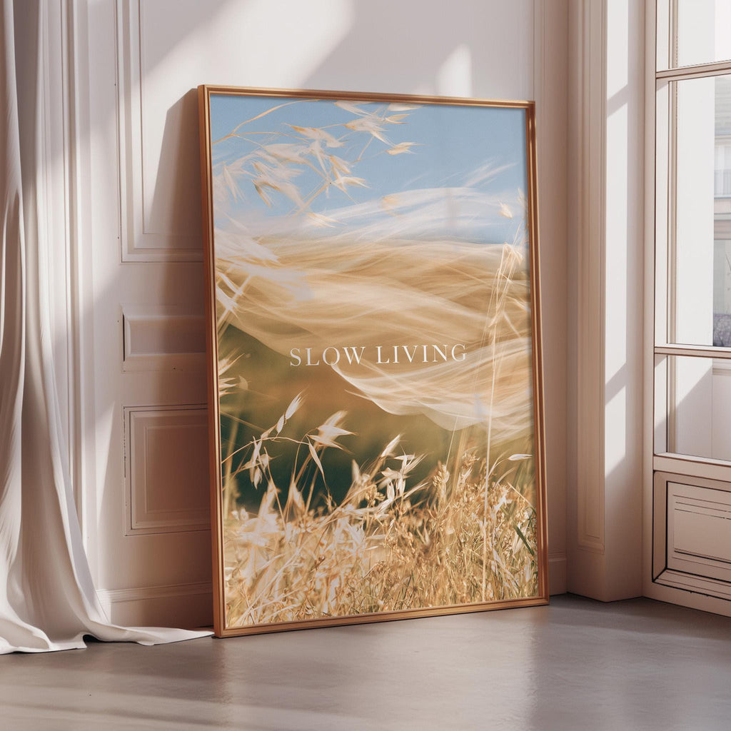 a large framed poster with a serene landscape of wheat fields and a blue sky, accompanied by the text "SLOW LIVING" in the center.